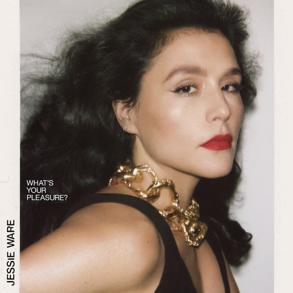 The album cover to Jessie Ware's What's Your Pleasure. Singer Jessie Ware is pictured looking at the camera from the side. Her hair is flowing back from her made-up face. She is wearing a large chain like necklace and has on a black blouse. 
